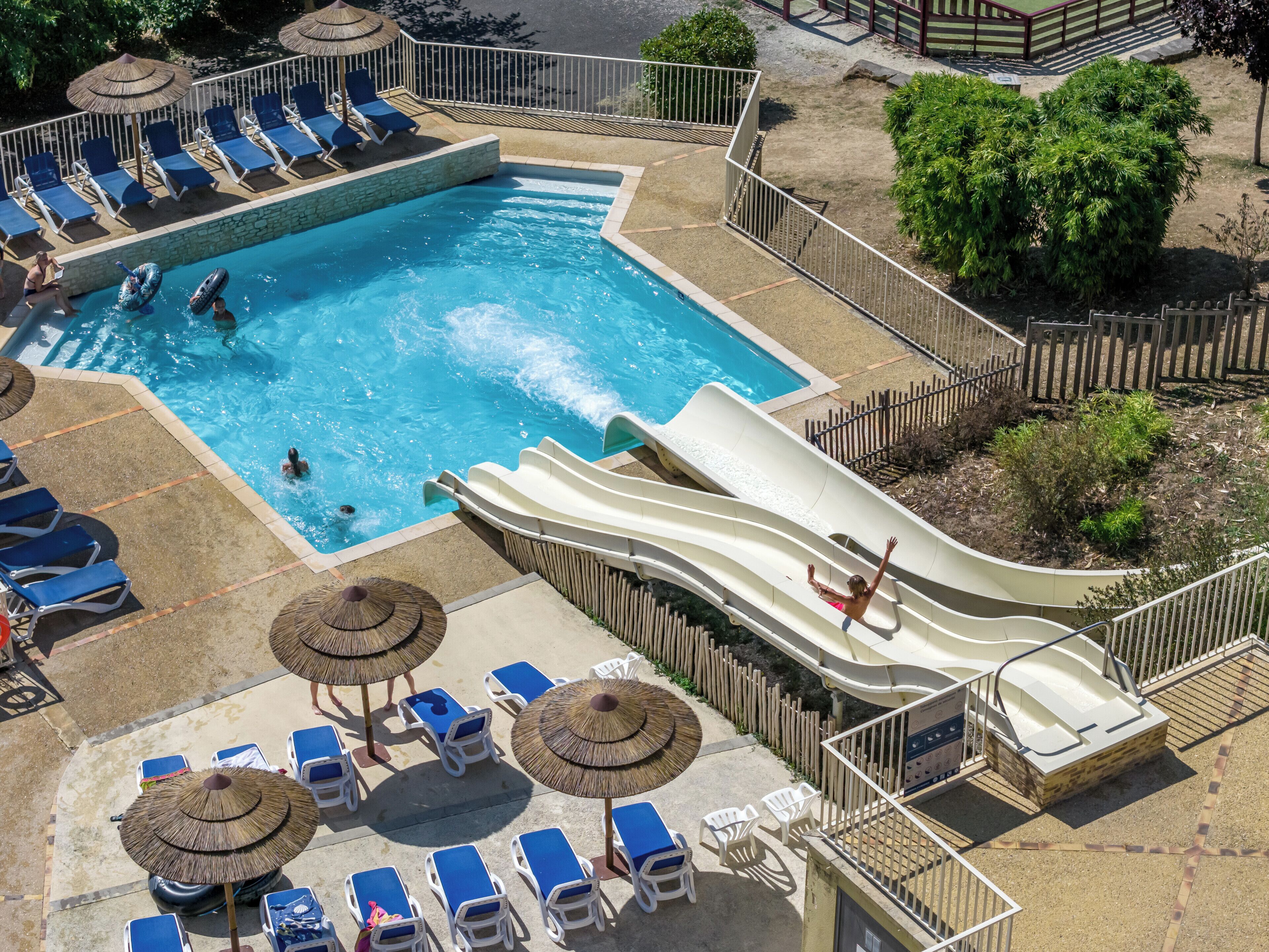 A swimming pool with a water slide, lounge chairs, and umbrellas.