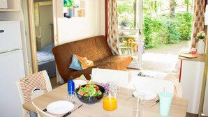 A cozy room with a brown sofa, a dining table with a salad, a jug of orange juice, and a refrigerator. - Truffe - Chalet confort 3 – 6p (8) (Saint-Geniès)