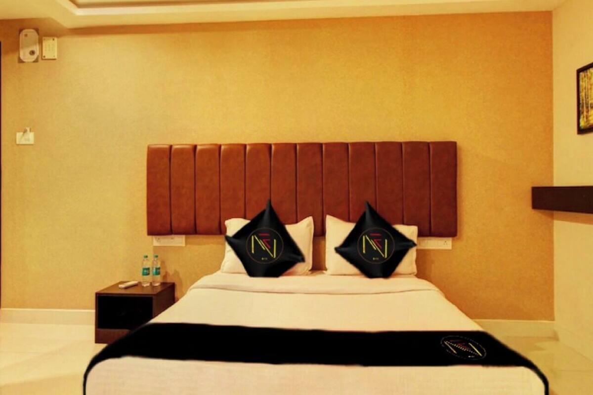 Una camera d'albergo con un letto grande, una ventola a soffitto e un comodino con una bottiglia d'acqua.