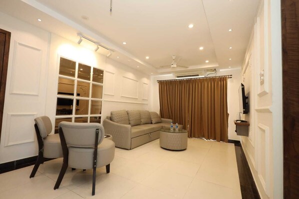 A modern living room with a sofa, armchairs, a glass coffee table, and a built-in shelving unit. - 7th Heaven Hotel Apartments (Manipal)