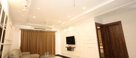 A modern living room with a sofa, armchair, and coffee table. There is a TV mounted on the wall and a wooden door.