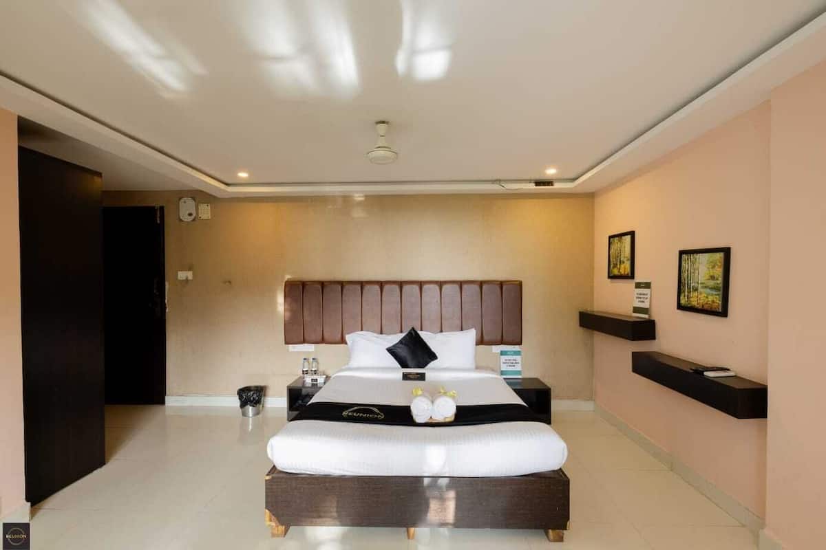 Una moderna camera d'albergo con un letto grande, un comodino, una mensola a muro e una porta che dà su un'altra stanza.