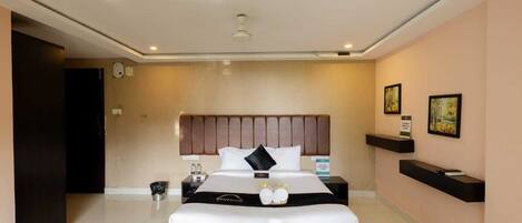 A modern hotel room with a large bed, a bedside table, a wall-mounted shelf, and a door leading to another room.