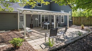 A covered patio with a table and chairs, surrounded by a wooden fence and a garden bed.