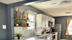 A modern kitchen with a granite countertop, white cabinets, and a built-in microwave. There are two bar stools and a window with a view.