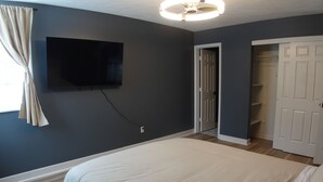 A bedroom with a bed, a TV mounted on the wall, a door leading to a closet, and a ceiling fan.
