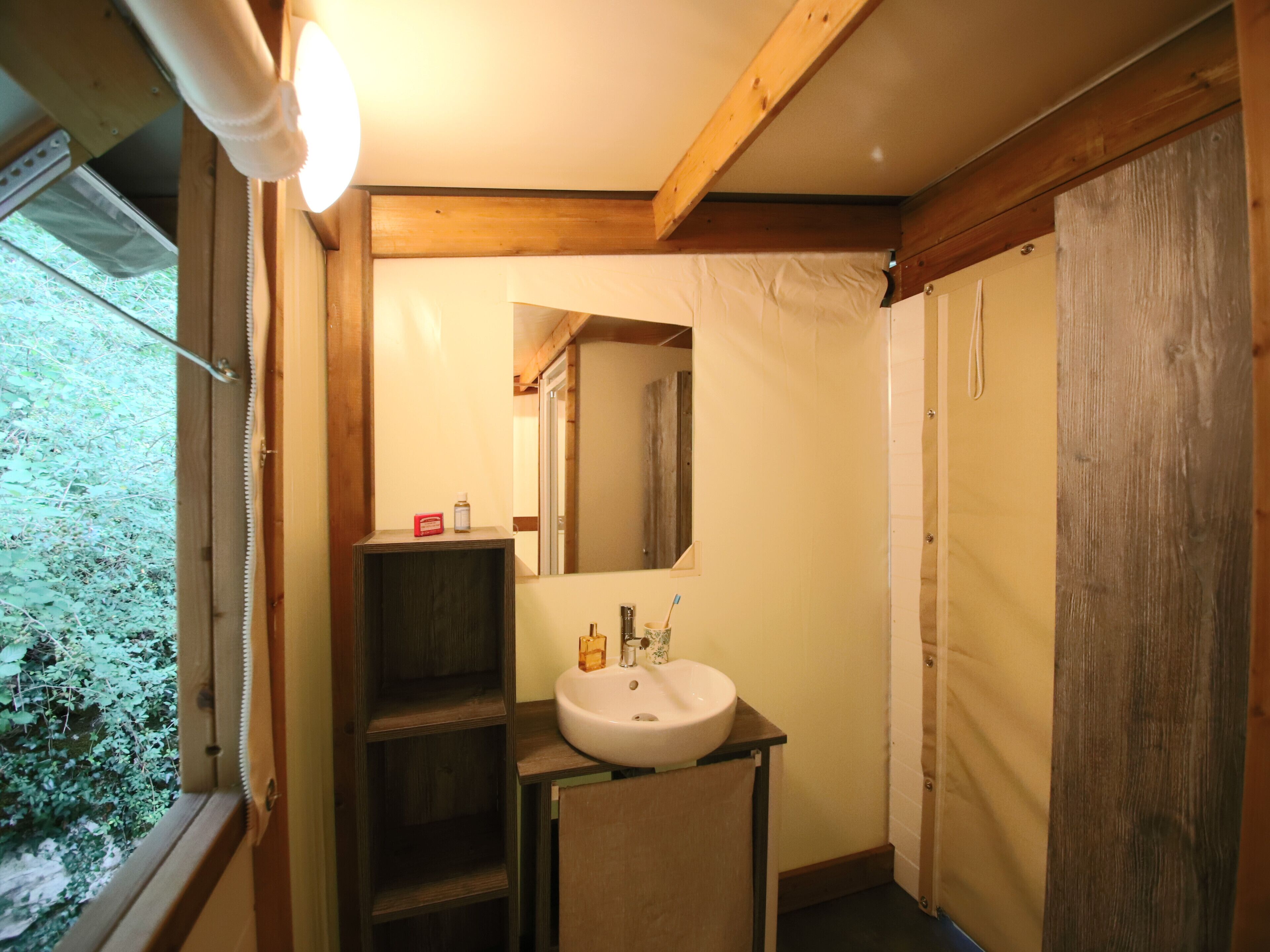 Uma casa de banho com teto de madeira, lavatório branco, espelho e janela com vista para vegetação.