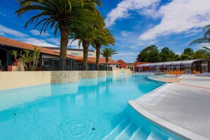 A swimming pool with clear blue water, surrounded by palm trees and lounge chairs. - Bela - Privilège 2 – 4p (Anglet)