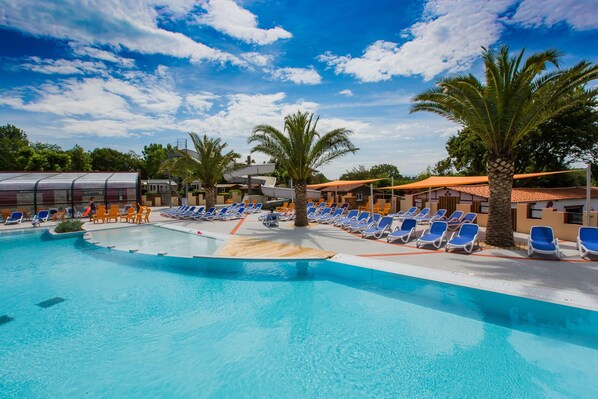 A swimming pool with blue and white lounge chairs, palm trees, and a clear sky. - Bela - Privilège 2 – 4p (Anglet)