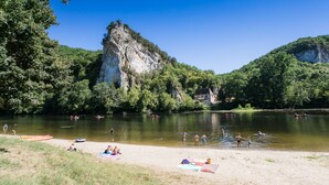 A riverside beach with kayaks, people swimming, and a house in the background. - Truffe - Privilège 2 - 4p (2) (Saint-Geniès)