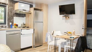 A modern kitchen with a dishwasher, refrigerator, and a dining area with a table and chairs. - Truffe - Privilège 2 - 4p (2) (Saint-Geniès)