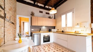 Une cuisine compacte avec des meubles blancs, un four encastré, un four à micro-ondes et un luminaire suspendu.