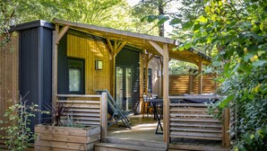 Een houten chalet met een overdekt terras, buitenmeubels en een kleine tuin.
