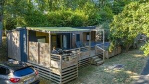 Een klein houten vakantiehuisje met een terras en een auto in de buurt.