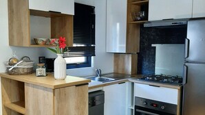 Kompakti keittiö, jossa on puukalusteet, sisäänrakennettu astianpesukone, kaasuliesi ja pieni oleskelualue.