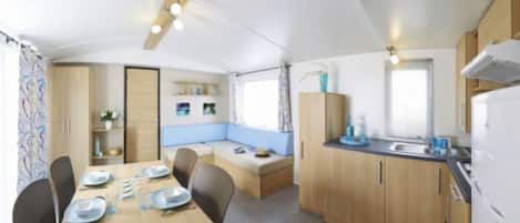 A compact kitchen with wooden cabinets, a dining table set for four, and a built-in bench with cushions.