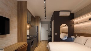 A modern hotel room with a wooden desk, a bed, a TV, a kitchen area, and a mirror. - Haus Mitre Vila Clementino by Wecare (São Paulo)