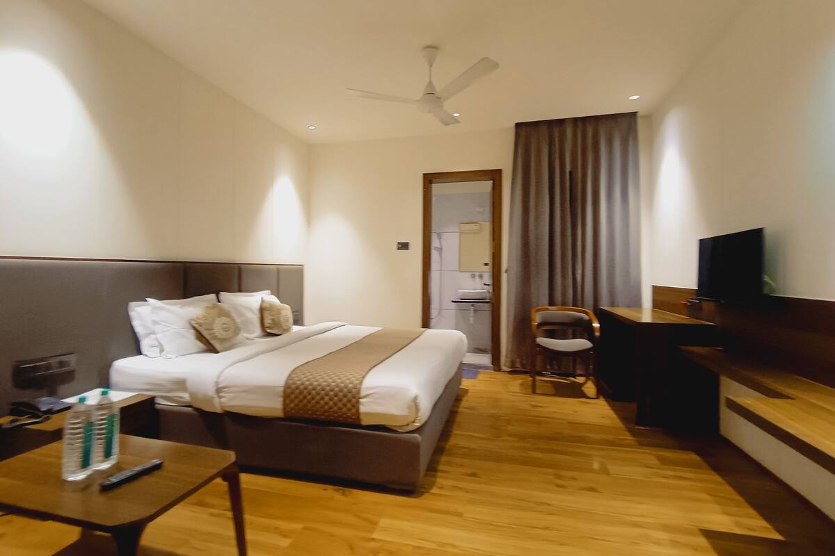 A hotel room with a bed, a desk, a chair, a television, and a ceiling fan.