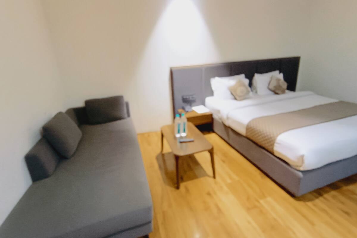 A hotel room with a bed, a sofa, a nightstand, and a bedside table.