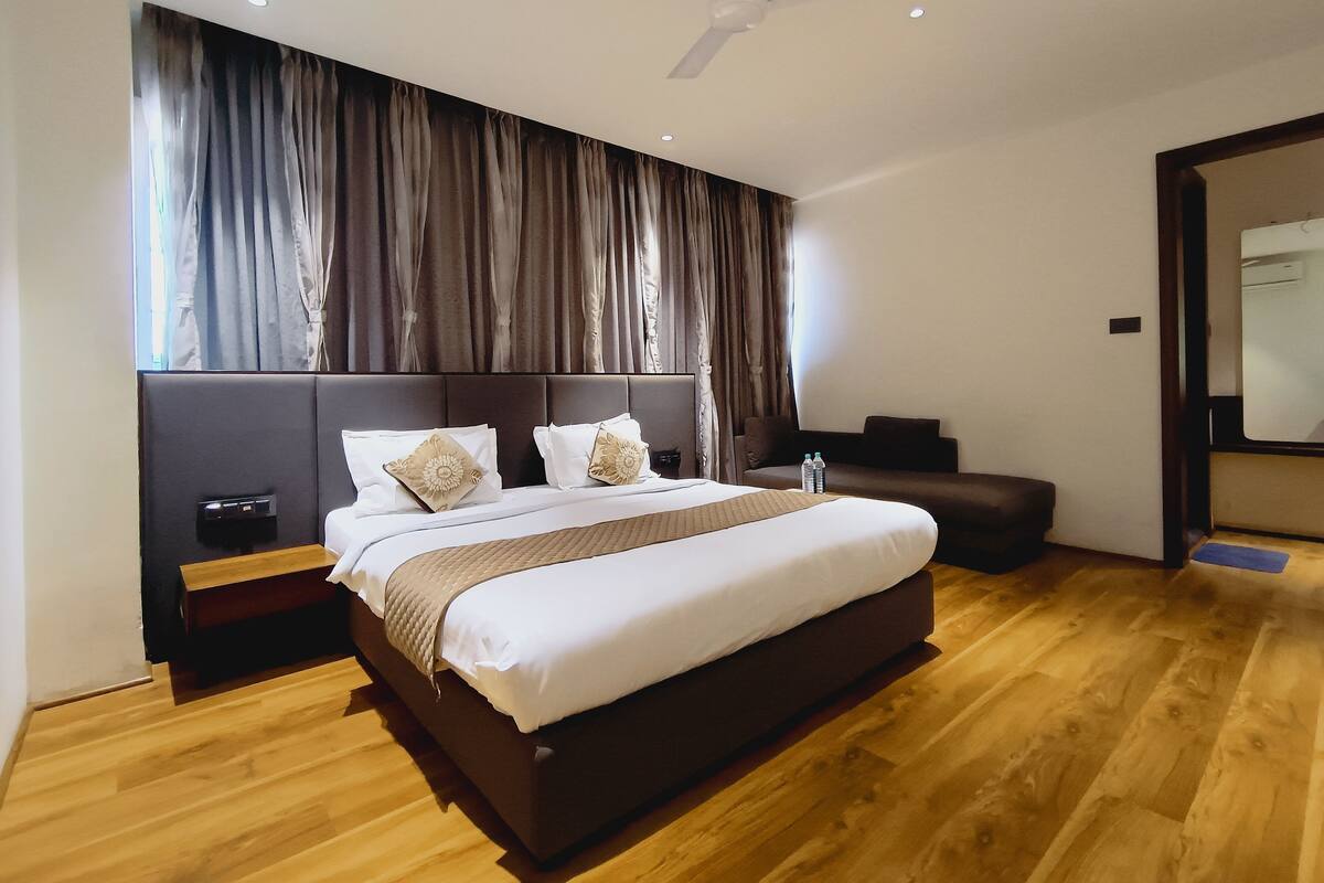 A modern hotel room with a large bed, a headboard, a bedside table, a nightstand, a ceiling fan, and a large window with curtains.