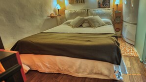 Una cama bien hecha con colcha verde y blanca, una mesita de noche con lámpara y una pared decorada con cuadros.
