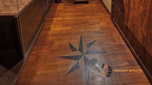Un estrecho pasillo con suelo de madera, diseño de piso con motivos de estrellas y estanterías llenas de libros y objetos varios.