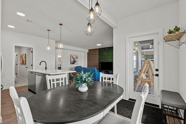 A modern kitchen with white cabinetry, a dark wooden dining table, and pendant lighting.