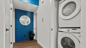 A laundry room with a blue accent wall, a round mirror, and stacked washing machines. - Bright, new suite 10 min from Calgary (Okotoks)