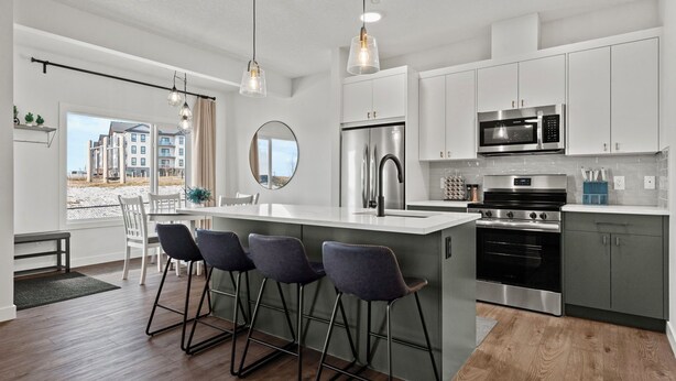 A modern kitchen with white cabinets, stainless steel appliances, and a large island with bar stools. - Bright, new suite 10 min from Calgary (Okotoks)