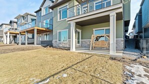 A row of modern multi-story homes with balconies, a grassy yard, and construction materials on the ground. - Bright, new suite 10 min from Calgary (Okotoks)