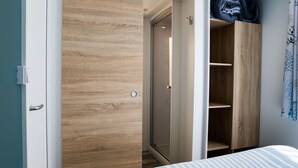 A bedroom with a wooden wardrobe, a bed with striped bedding, and a blue and white striped curtain. - Palmyre - Confort 3 - 7p (14) (Les Mathes)
