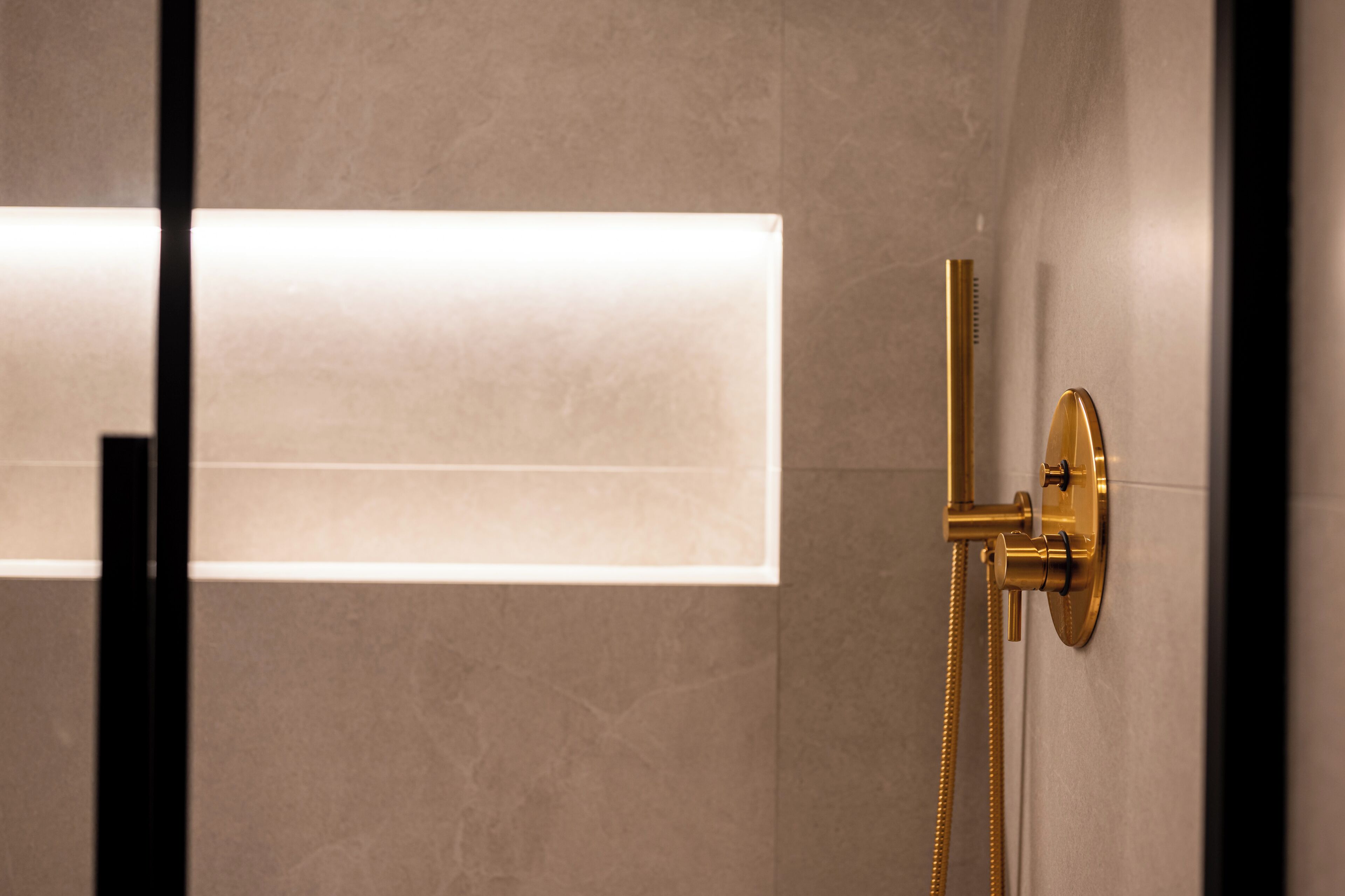 Une salle de bain moderne avec une pomme de douche dorée et un luminaire fixé au mur.