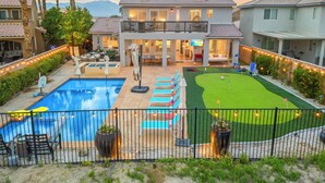 Uma casa de dois andares com piscina, quadra de tênis e gramado bem cuidado.