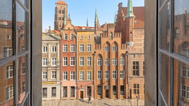 A view from a window of a building with a brick facade, a tower with a spire, and a clear sky. - Louise Apartment Old Town Długa Street (Gdańsk)