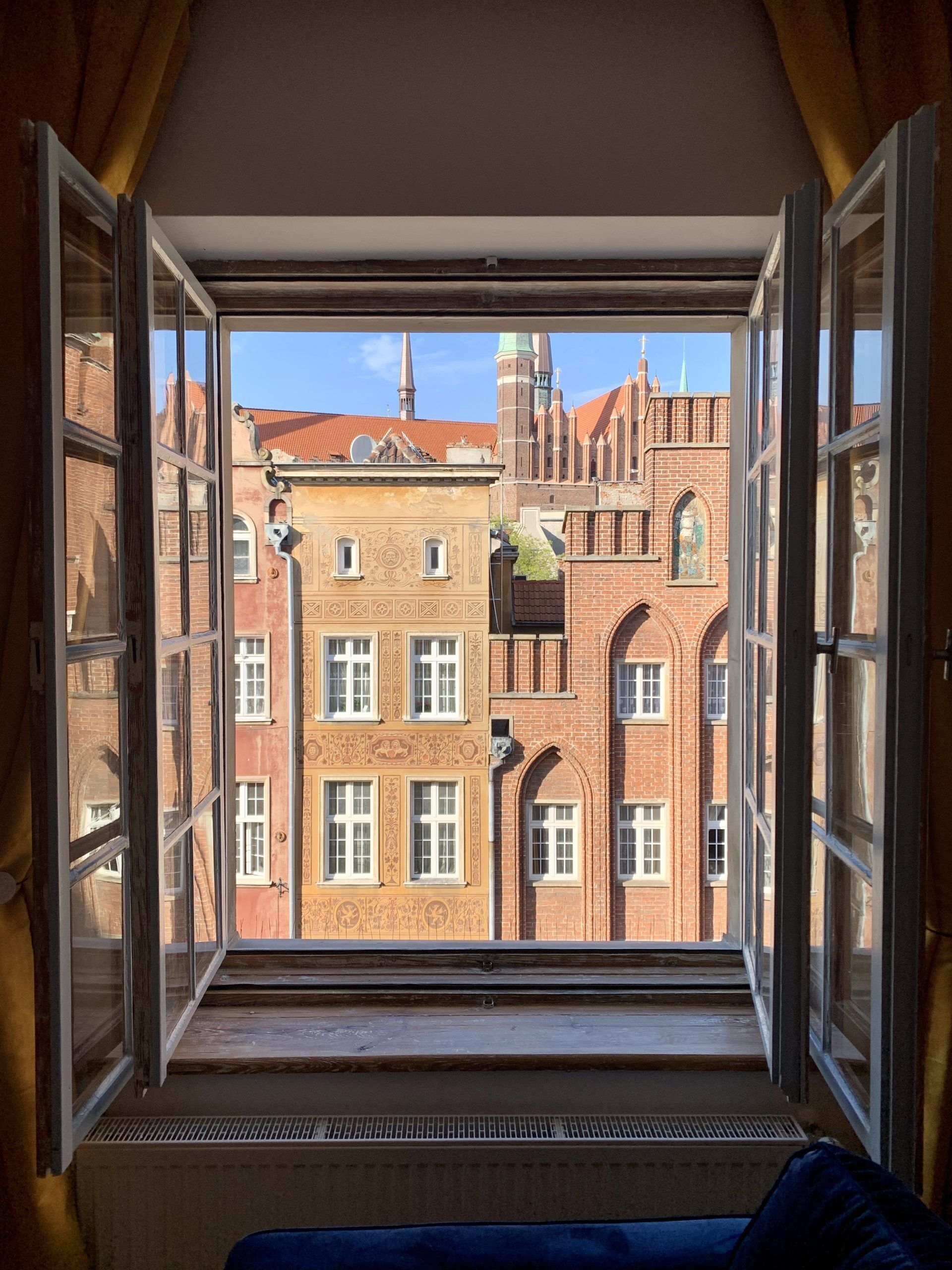 Ventana abierta con vistas a un edificio histórico de ladrillo rojo y múltiples ventanales.