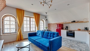 A modern living room with a blue sofa, a round coffee table, and large windows with yellow curtains. - Louise Apartment Old Town Długa Street (Gdańsk)