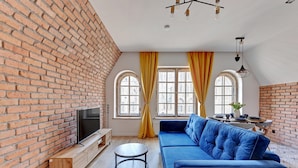 A modern living room with a brick wall, a blue sofa, a TV on a wooden stand, and a round coffee table. - Louise Apartment Old Town Długa Street (Gdańsk)
