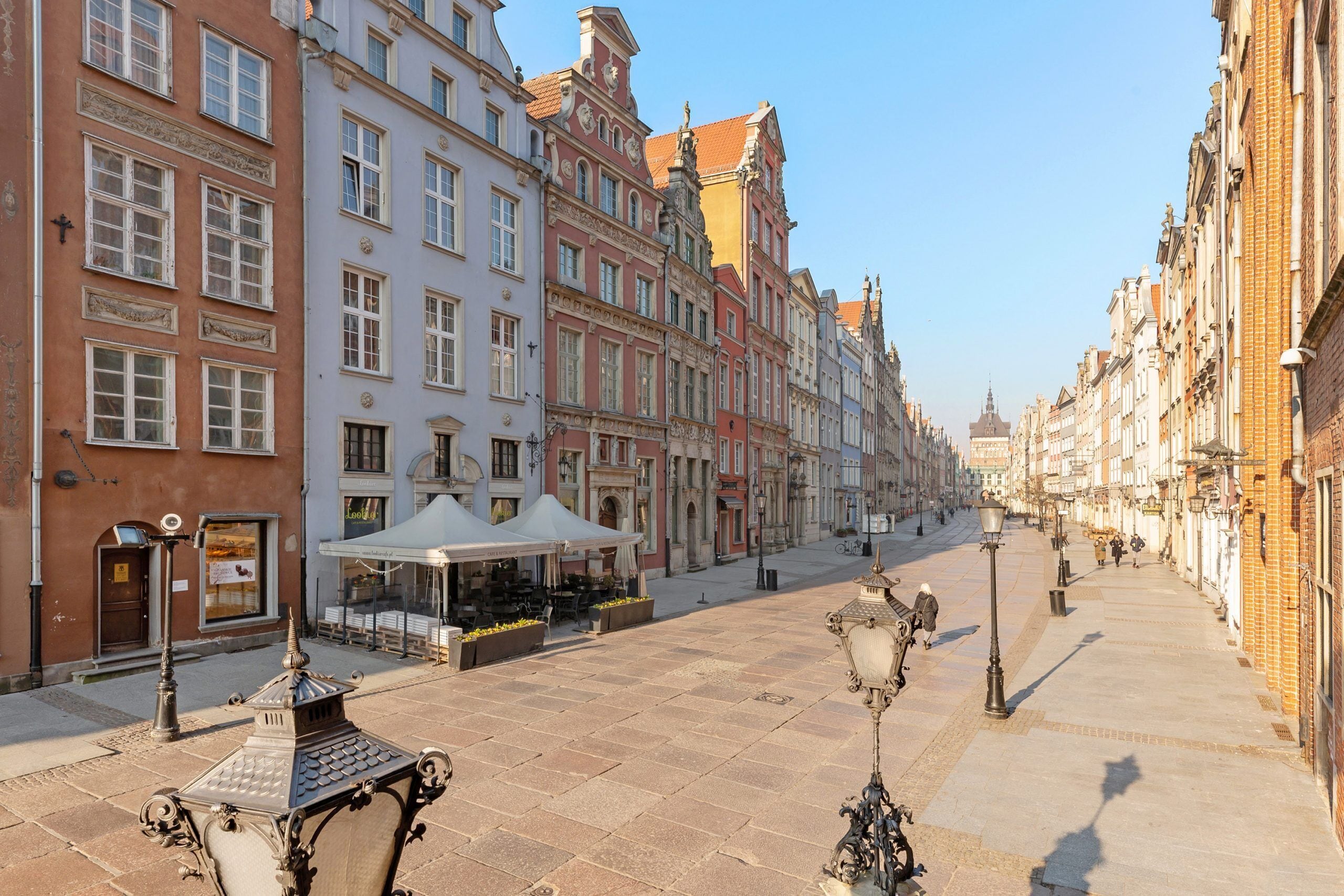 A historic street lined with colorful buildings, a café with outdoor seating, and ornate street lamps.