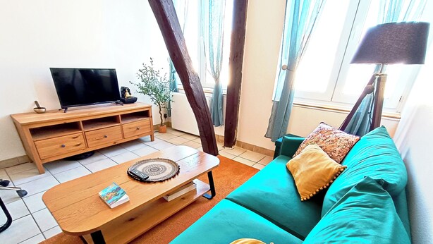A living room with a teal sofa, wooden coffee table, and a TV on a wooden stand. - Apartment 7 - Cozy, near the train station and downtown, free parking (Châlons-en-Champagne)