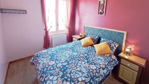 A bedroom with a floral bedspread, a headboard with a leaf pattern, two bedside tables with lamps, and a window with curtains. - Apartment 7 - Cozy, near the train station and downtown, free parking (Châlons-en-Champagne)
