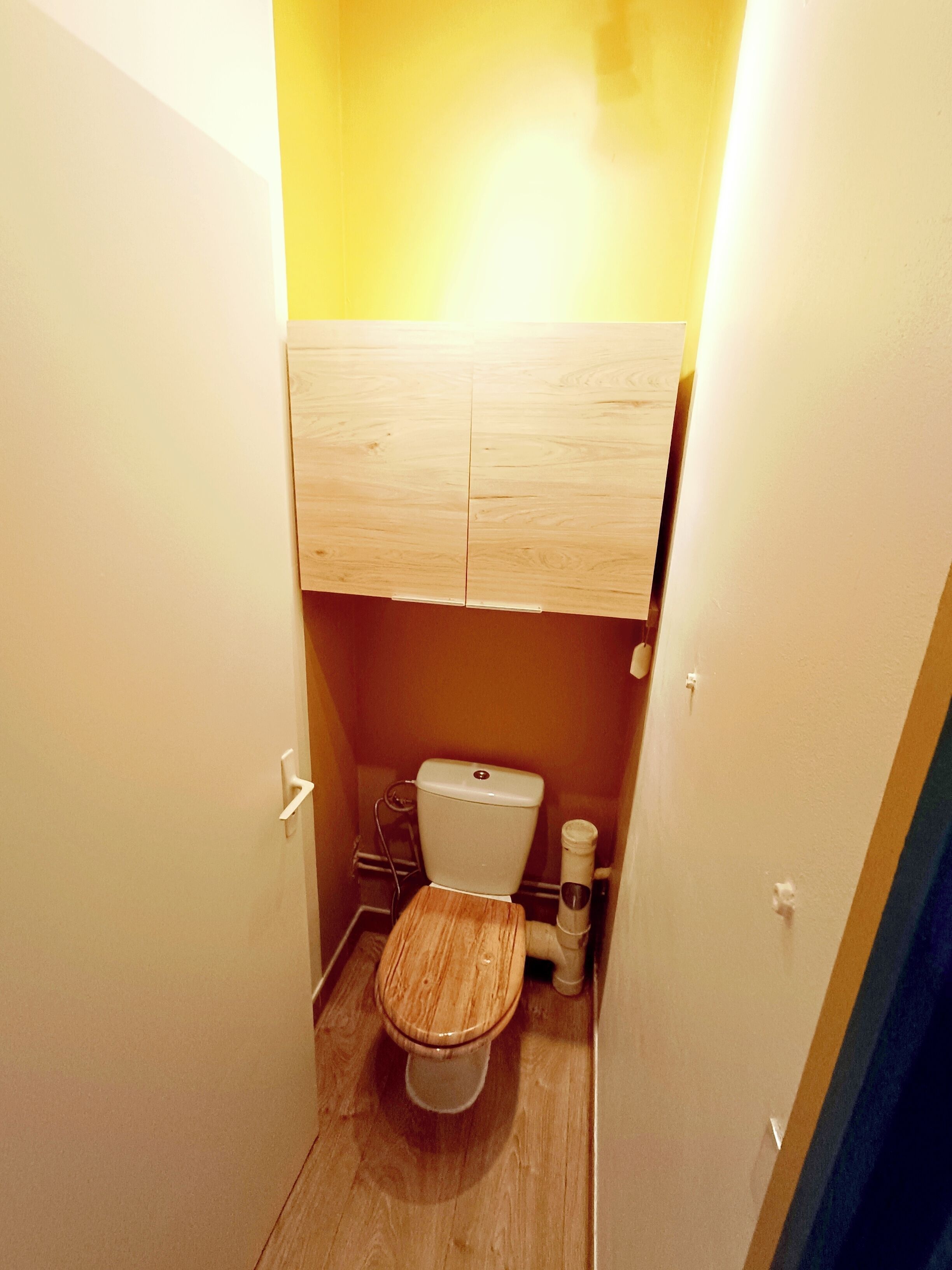 A compact bathroom with a wooden toilet, a white sink, and a cabinet above the toilet.