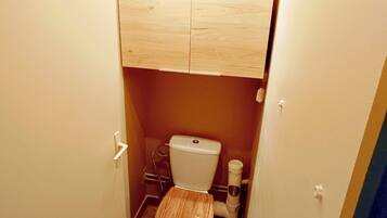 A compact bathroom with a wooden toilet, a white sink, and a cabinet above the toilet.