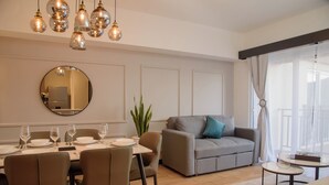 A modern living room with a dining area, a grey sofa, and a round mirror on the wall.