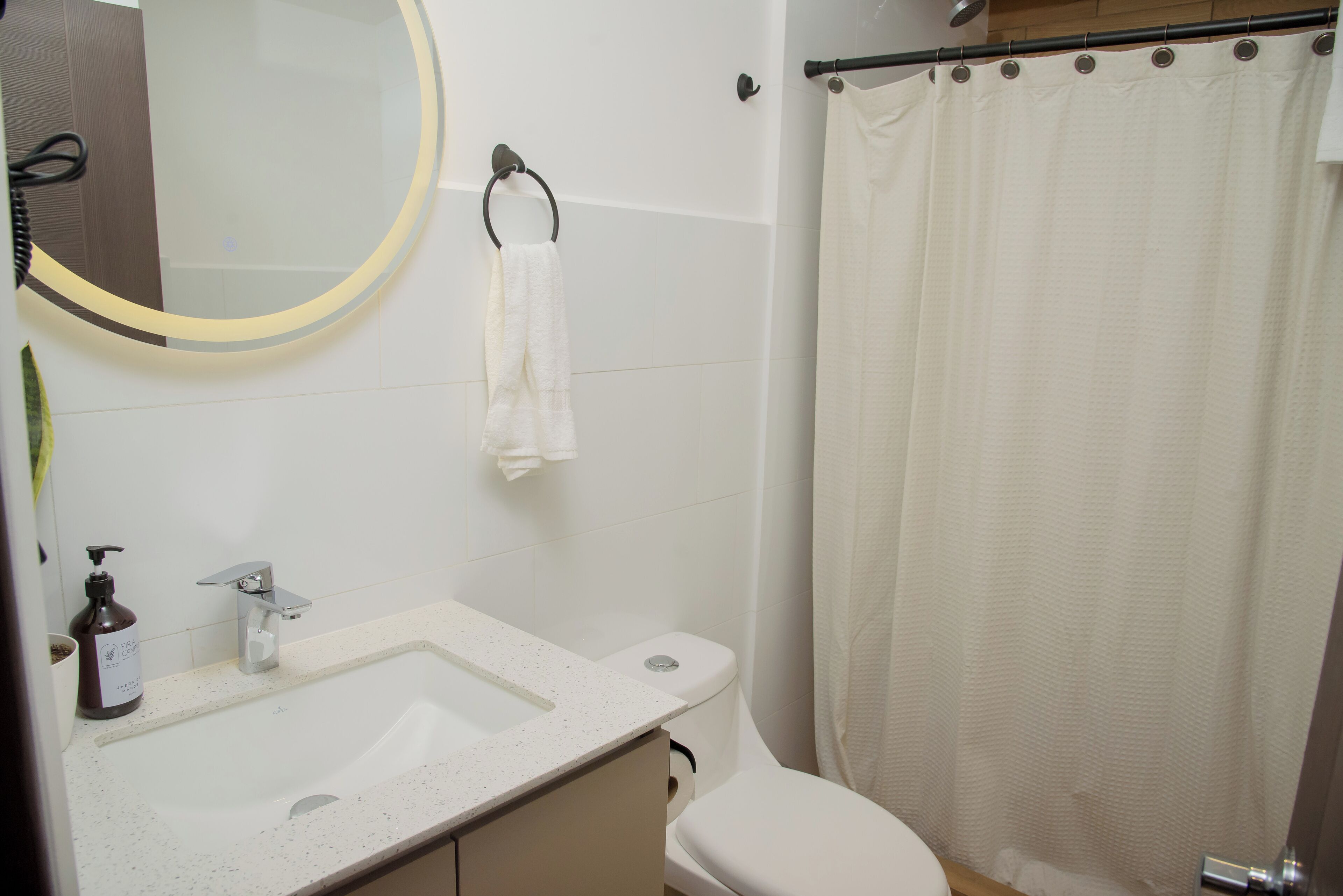 A bathroom with a white sink, a toilet, a mirror with a light, and a shower curtain.