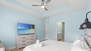 Un dormitorio con cama, televisor, ventilador de techo y una puerta que da a otra habitación.