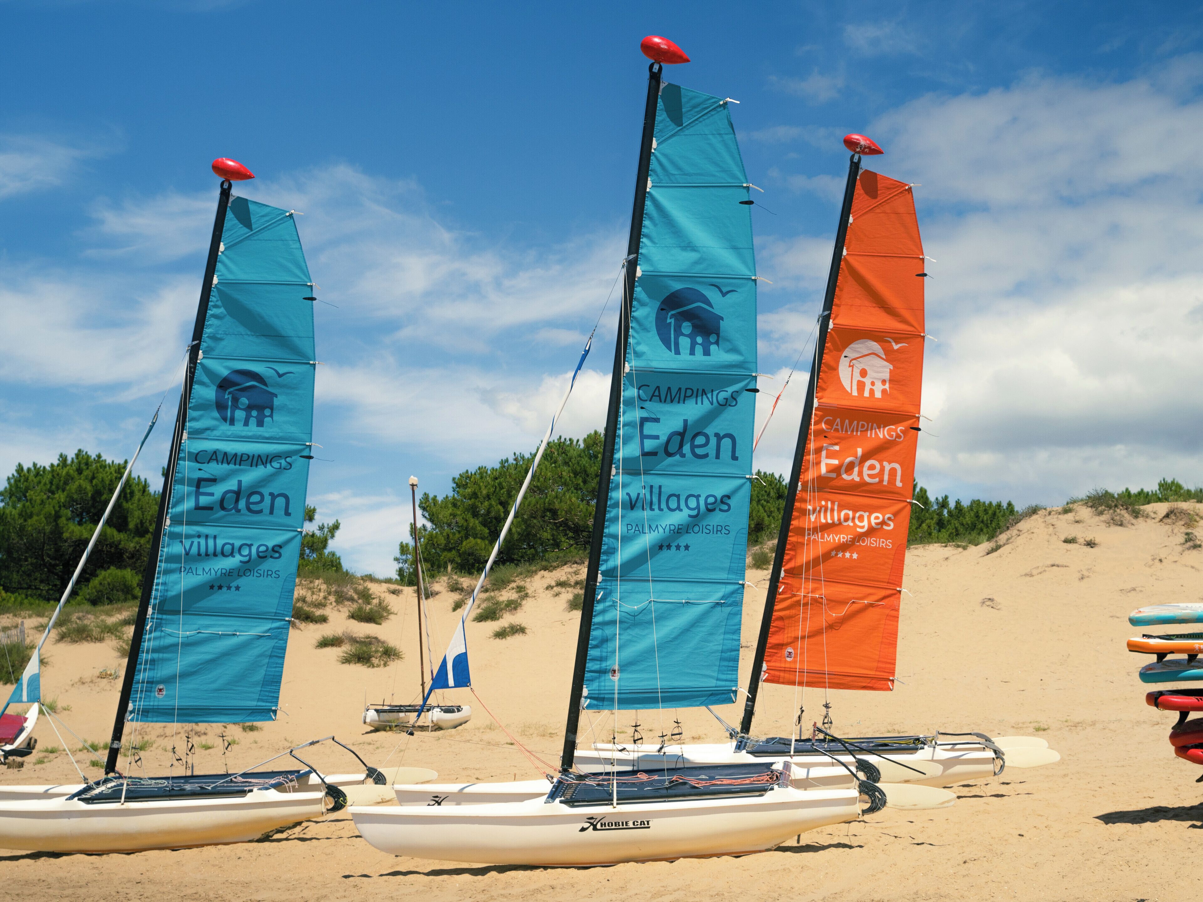 Drei Segelboote mit Flaggen an einem Sandstrand.