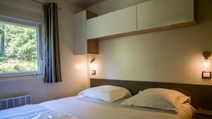 A hotel room with a bed, a window with curtains, a wall-mounted light fixture, and a radiator. - Palmyre - Privilège 2 - 4p (7) (Les Mathes)