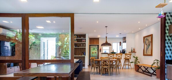 A modern kitchen with a dining area, wooden furniture, and a view through a glass door. - Casa com jacuzzi e rooftop by Wecare (Bertioga)