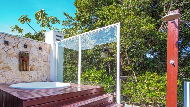 A stone exterior wall, a glass door, and a wooden deck. - Casa com jacuzzi e rooftop by Wecare (Bertioga)