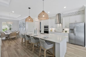 A modern kitchen with white cabinetry, a stainless steel refrigerator, and a central island with bar stools. - New Home w/ Pool at The National in Ave Maria FL (Ave Maria)